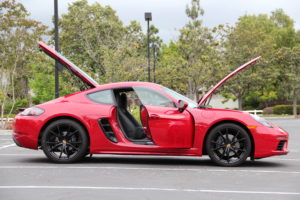 A 2018 Porsche 718 Cayman base model, photographed from a side profile with its hood, trunk and doors wide open showing some of the black interior