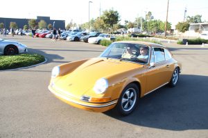 A Porsche 911 classic in yellow color driving through a parking lot