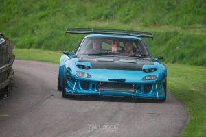 A modified 3rd generation Mazda RX7, teal color with black accents, front view