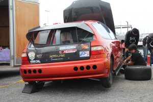 An orange Honda Civic EG hatchback being prepared for a drag racing event