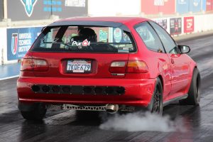 A red Honda Civic EG hatchback does a burnout on a drag strip