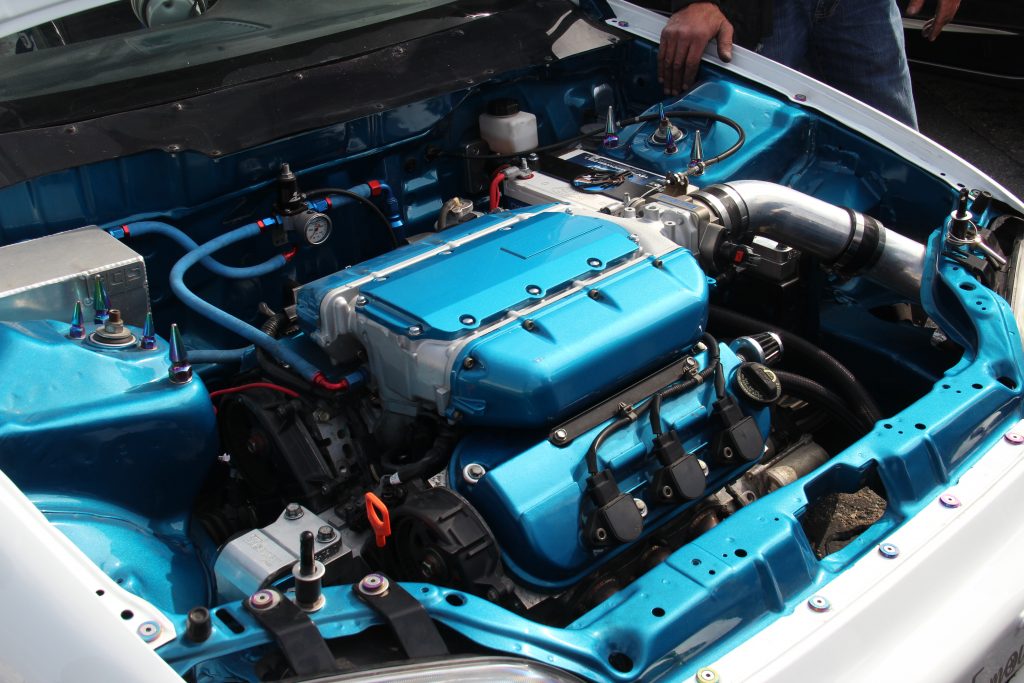 The engine bay of a car engine swapped with a Honda Odyssey engine, with teal accents