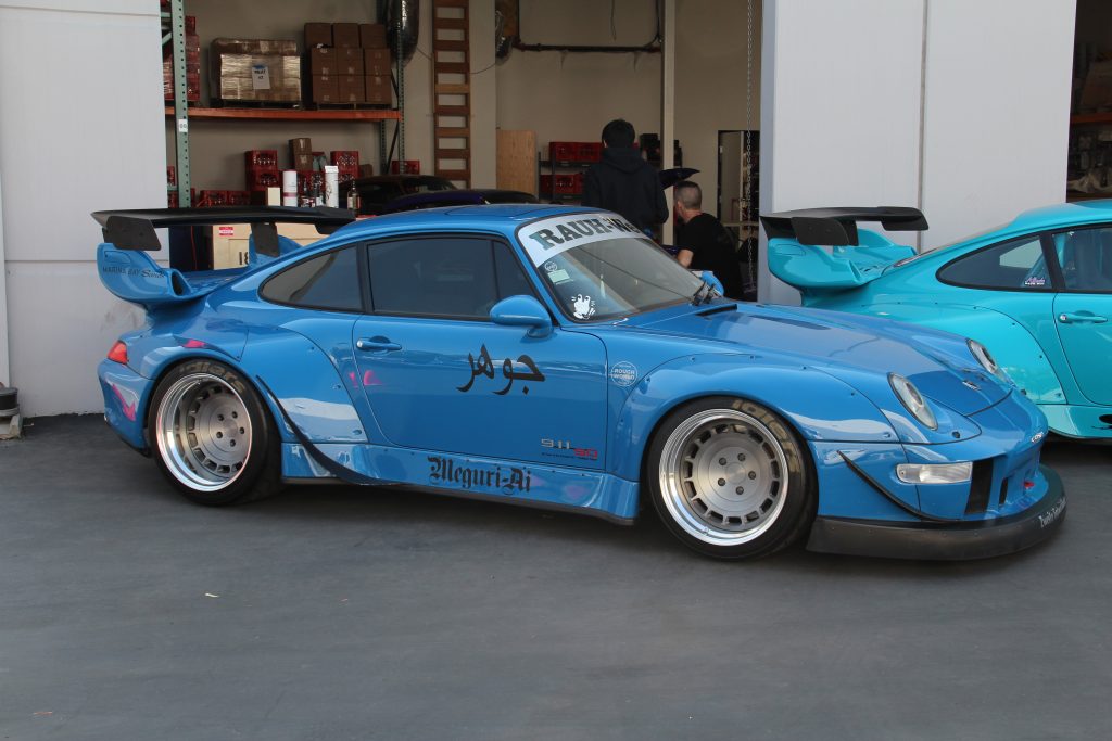 A RWB Porsche 993, nicknamed Meguri-Ai, painted blue, sits outside a warehouse.
